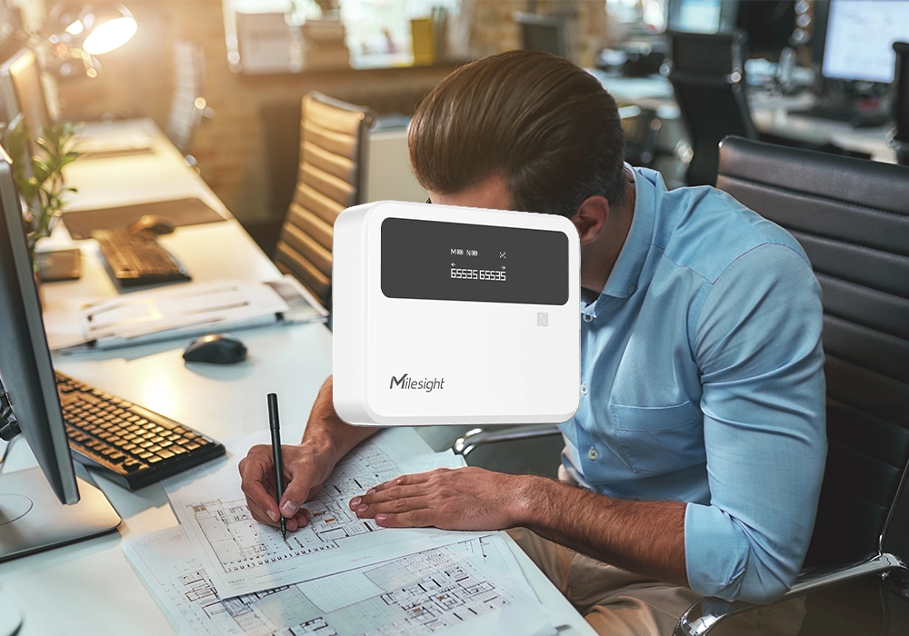 The Milesight Breakbeam people counter. The background is a man working at a desk in an office, drawing schematics on paper. The Milesight Breakbeam people counter. The background is a man working at a desk in an office, drawing schematics on paper.