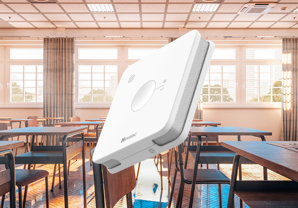 The Nexelec smart smoke alarm. The background is the interior of a classroom.
