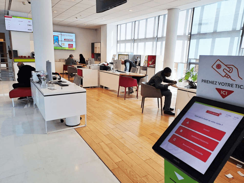 Wide shot of the bank’s reception area with TIKK 15 kiosk and player screen managing customer flow. Wide shot of the bank’s reception area with TIKK 15 kiosk and player screen managing customer flow.
