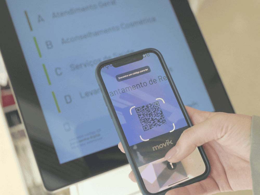A visitor at Loureiro Basto Pharmacy scanning a QR code on the Tiik Kiosk to take a digital ticket. A visitor at Loureiro Basto Pharmacy scanning a QR code on the Tiik Kiosk to take a digital ticket.