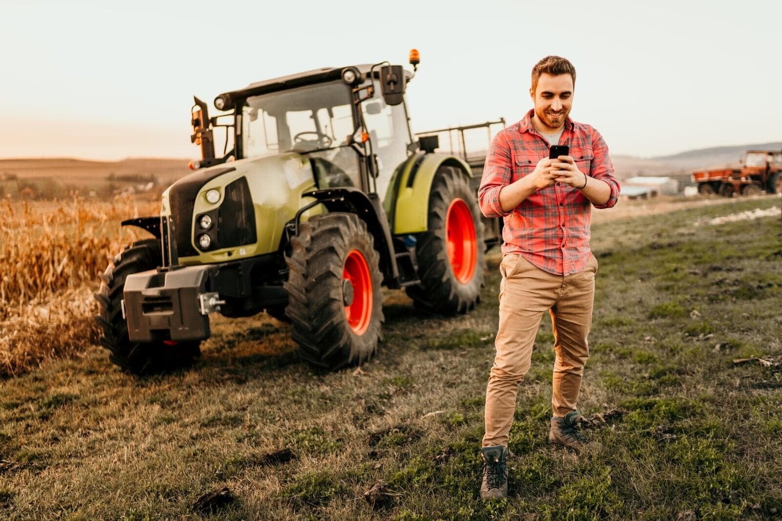 Agriculteur heureux avec son smartphone dans la main devant son tracteur dans un champs Agriculteur heureux avec son smartphone dans la main devant son tracteur dans un champs