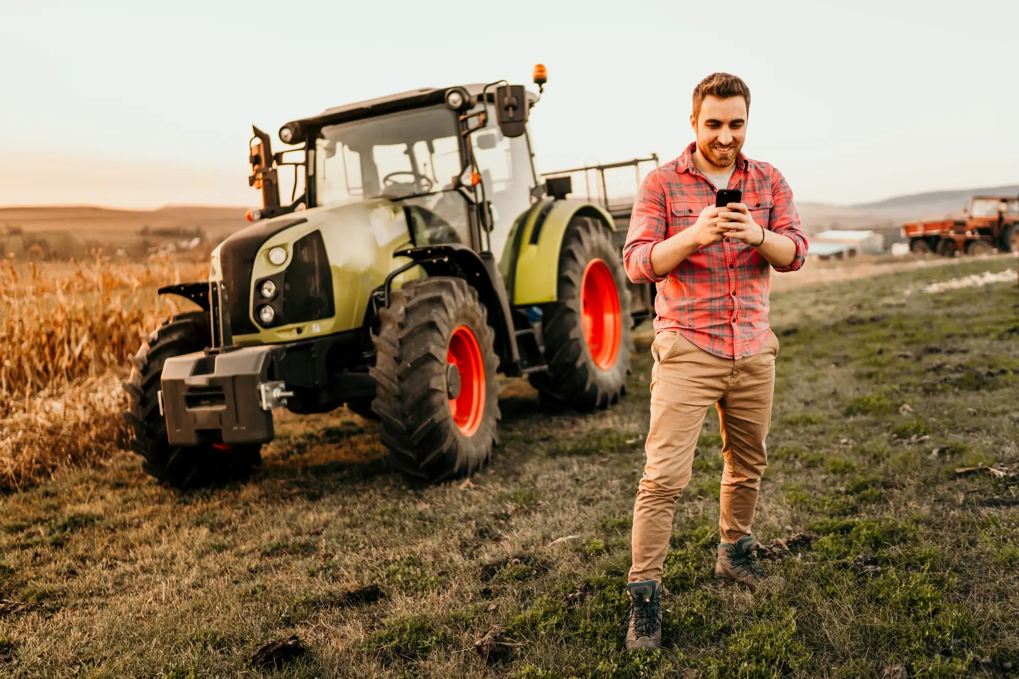 Agriculteur heureux avec son smartphone dans la main devant son tracteur dans un champs