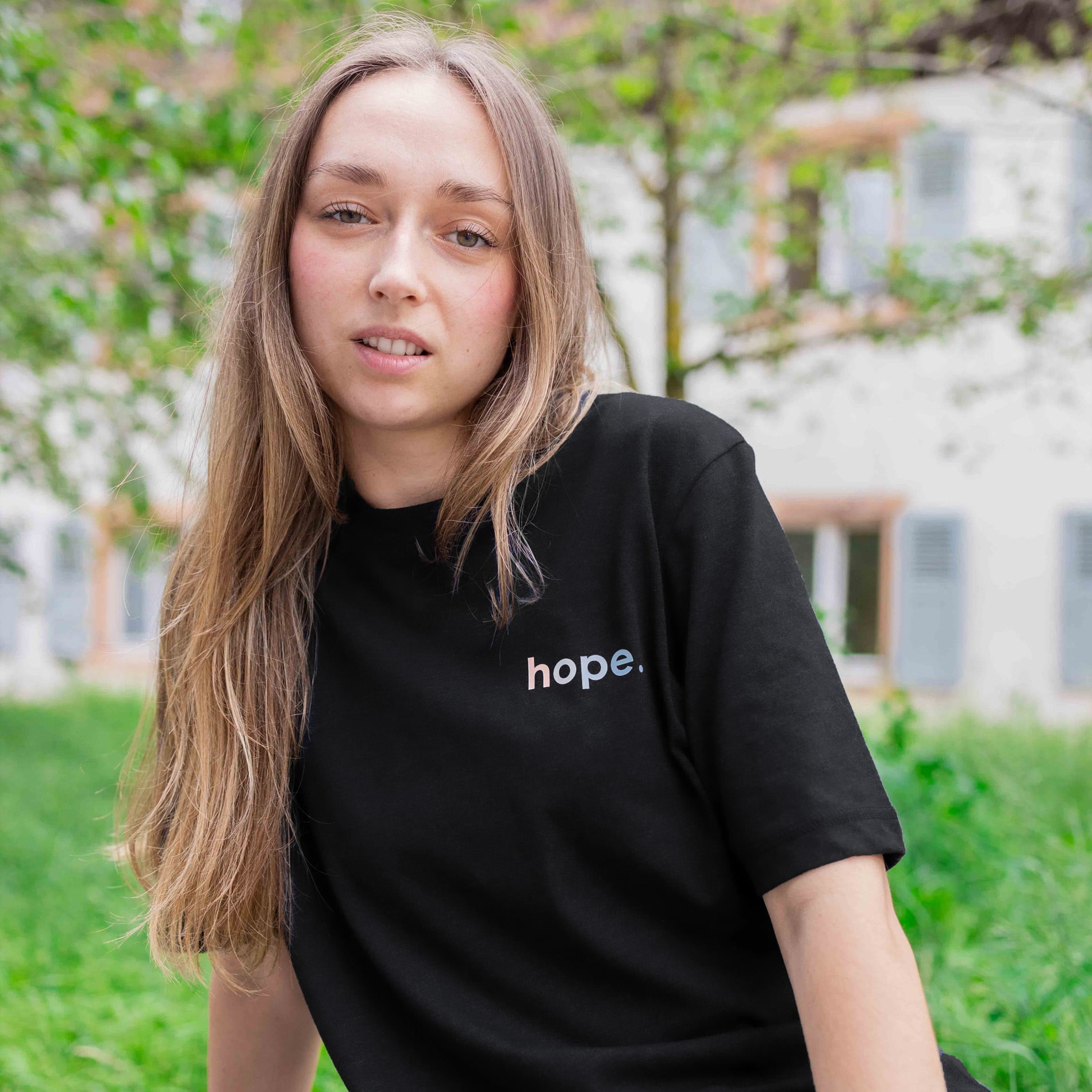 Hope T-Shirt in Schwarz mit Schriftzug hope., getragen von einer Frau im Grünen vor einem Haus